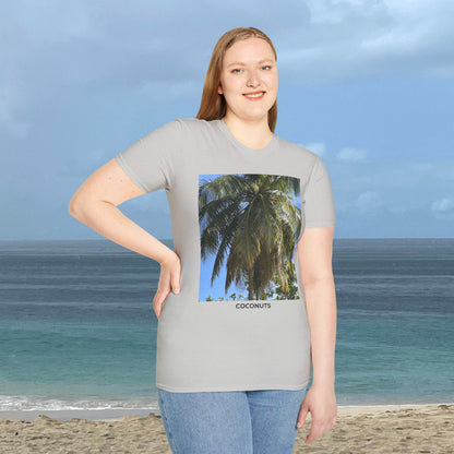 Woman standing by the ocean wearing a light gray Coconut Tree T-shirt with a coconut palm photograph and “COCONUTS” printed on the front.