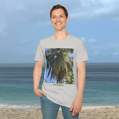 Man standing by the ocean wearing a light gray Coconut Tree T-shirt with a palm photograph and “COCONUTS” printed on the front.