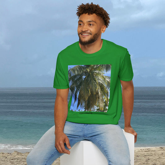 Man seated by the ocean wearing an Irish Green Coconut Tree T-shirt with a palm photograph and “COCONUTS” printed on the front.