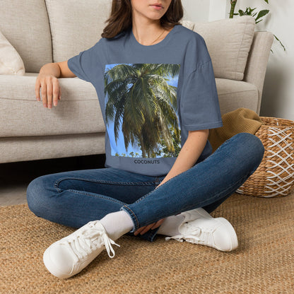 Woman seated indoors wearing a slate blue Coconut Tree T-shirt with a coconut palm photograph and “COCONUTS” printed beneath the image.