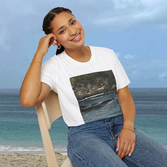 Woman seated by the ocean wearing a white Caribbean Coastal Sea Rocks T-shirt featuring a photograph of a rocky shoreline and ocean waves.
